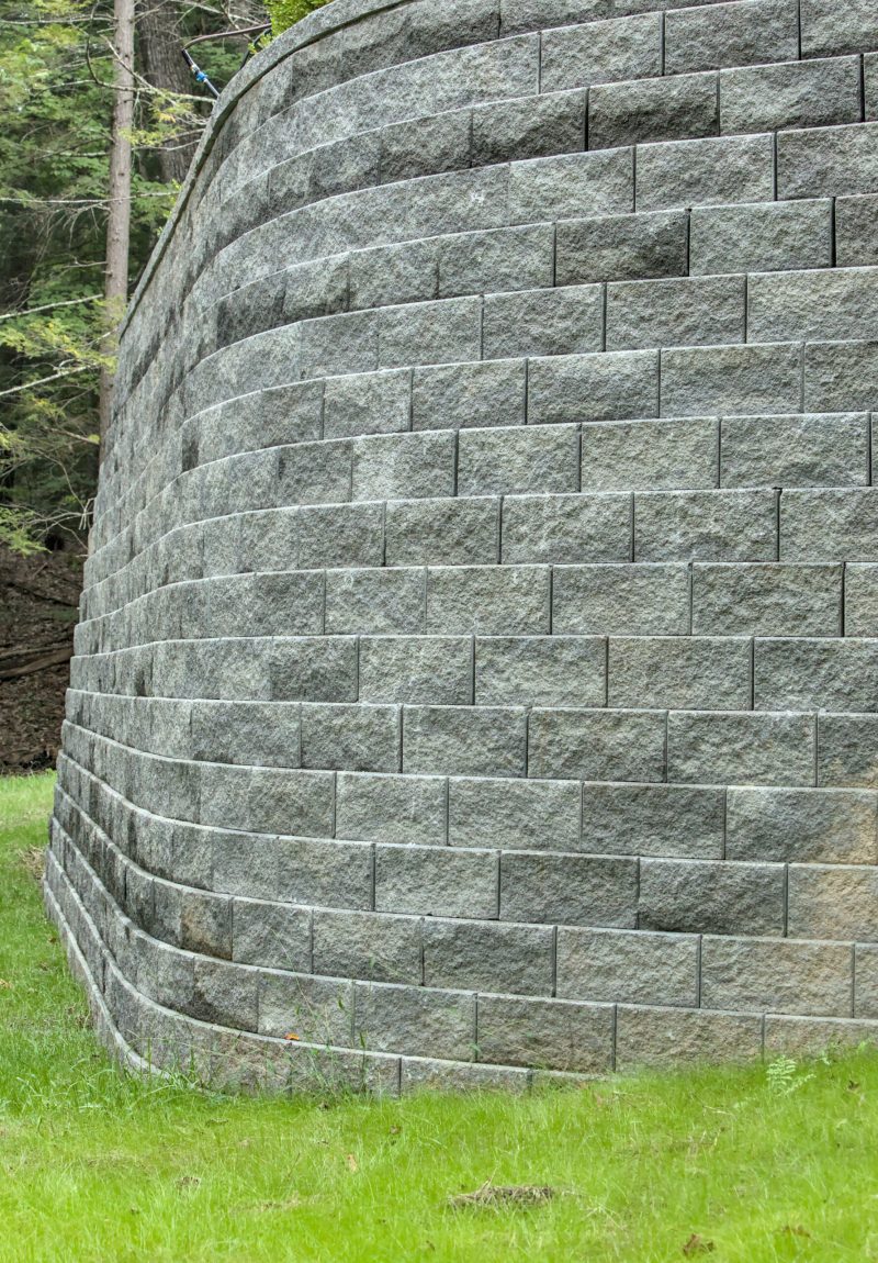 tall stone retaining wall (curved brick masonry) in house back yard (large gray supporting structure)